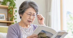 メガネをかけているものの本を見にくそうにしている白内障の高齢女性