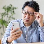 スマホが見にくく、メガネを持ち上げ顔をしかめる中年男性