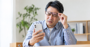 スマホが見にくく、メガネを持ち上げ顔をしかめる中年男性