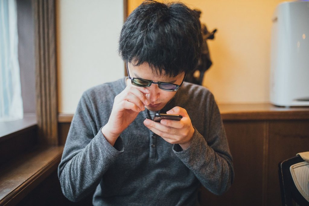 スマホを目に近づけて見ているメガネの男性